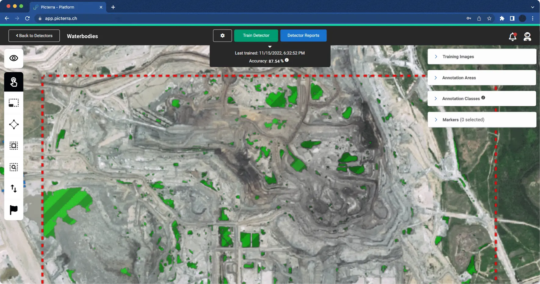 This image showcases the Picterra detector training interface applied to an industrial or mining site. Within a red dashed annotation area, several bright green polygons highlight identified "Waterbodies" across the excavated terrain. The top dashboard indicates the AI model's performance, showing a training accuracy of 87.54% as of November 2022. The interface includes tools for training the detector, viewing reports, and managing annotation classes, demonstrating how machine learning is used to automate the monitoring of environmental features in complex industrial landscapes.